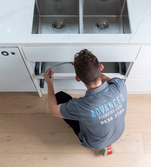 A Man Repairing a Sink in A Kitchen — Professional Plumbing Services in Sydney, NSW